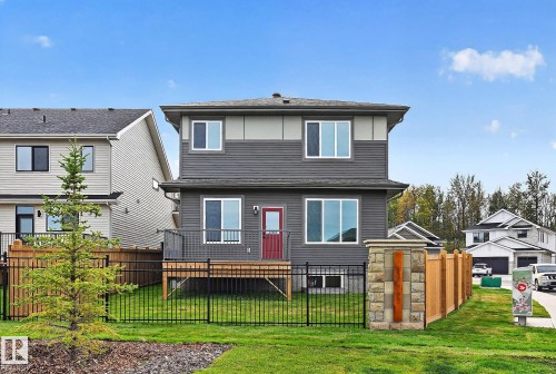 Two-story exterior with multi-toned siding, a rear deck, a red entry door, a black metal fence, and a wood privacy fence with stone pillars - 22 Sydwyck Circle, Spruce Grove, AB 