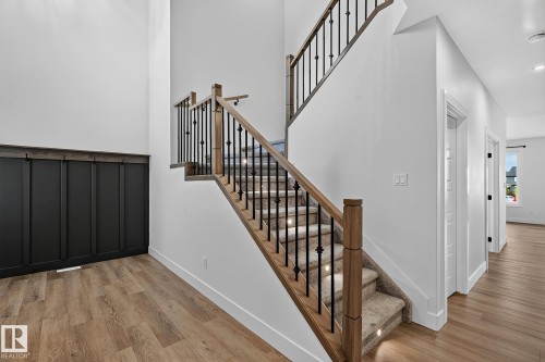 Wood-finish flooring throughout, with a carpeted staircase featuring decorative wrought iron balusters - 22 Sydwyck Circle, Spruce Grove, AB 