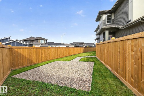 Private backyard featuring a full wood fence, green lawn, and a gravel patio area - 22 Sydwyck Circle, Spruce Grove, AB 
