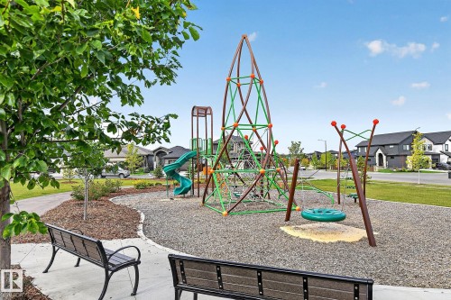 Community park featuring a play structure with a spiral slide, a climbing net, and a swing area, bordered by a walking path and seating - 22 Sydwyck Circle, Spruce Grove, AB 