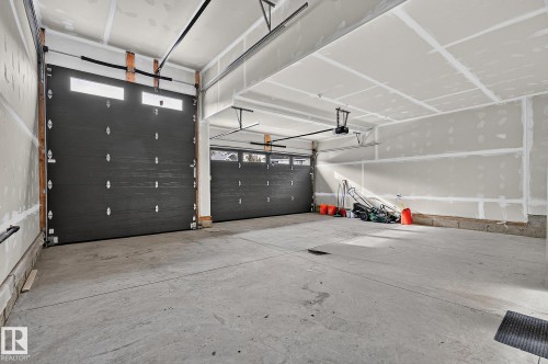 Spacious concrete-floored garage with two dark gray paneled overhead doors featuring windows - 22 Sydwyck Circle, Spruce Grove, AB 
