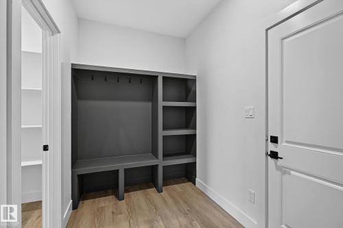Built-in mudroom bench with storage cubbies and coat hooks, wood-finish flooring, and a flat-panel door with black hardware - 22 Sydwyck Circle, Spruce Grove, AB 