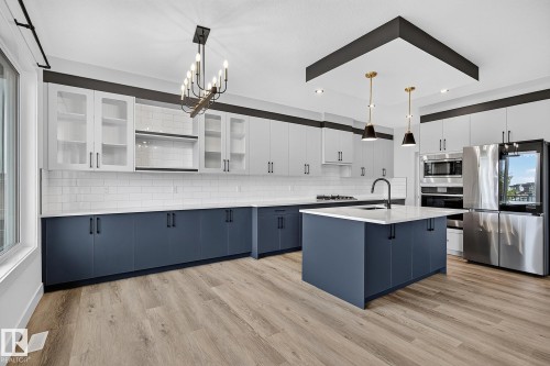 Spacious kitchen featuring an expansive island, stainless steel appliances, wood-finish flooring, white subway tile backsplash, and two-tone cabinetry - 22 Sydwyck Circle, Spruce Grove, AB 