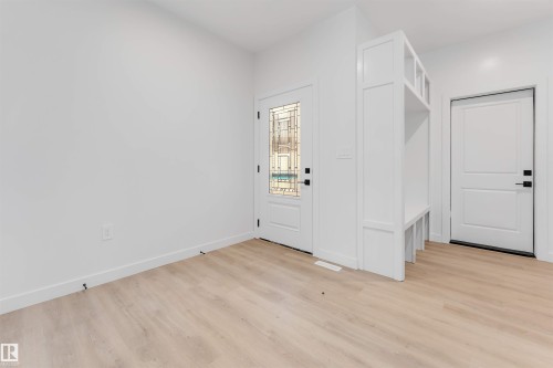 Light wood-finish flooring, white walls, decorative glass front door, built-in mudroom bench with shelving, and a solid panel interior door - 13 Trill Point(E), Spruce Grove, AB 