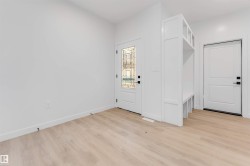 Light wood-finish flooring, white walls, decorative glass front door, built-in mudroom bench with shelving, and a solid panel interior door - 