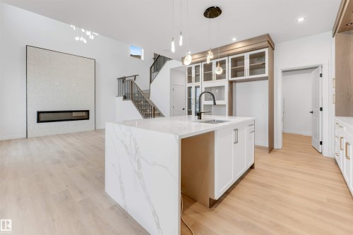 Open-concept living space with light wood-finish flooring, a contemporary fireplace, and a kitchen island featuring a waterfall countertop - 13 Trill Point(E), Spruce Grove, AB 