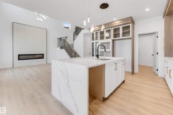 Open-concept living space with light wood-finish flooring, a contemporary fireplace, and a kitchen island featuring a waterfall countertop - 