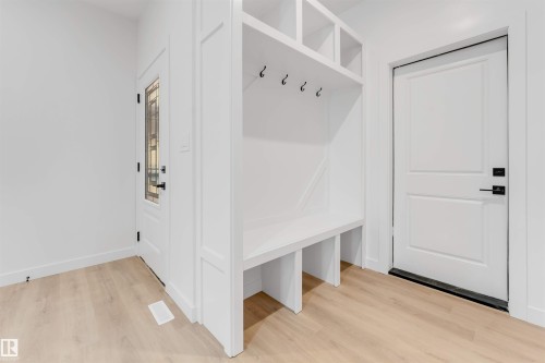 Built-in white storage bench with upper cubbies and coat hooks, light wood-finish flooring, and white paneled doors - 13 Trill Point(E), Spruce Grove, AB 