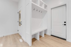 Built-in white storage bench with upper cubbies and coat hooks, light wood-finish flooring, and white paneled doors - 