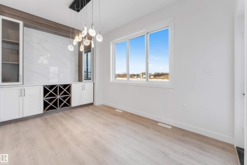 Built-in cabinetry with glass-front uppers, an integrated wine rack, and a marble-patterned backsplash - 13 Trill Point(E), Spruce Grove, AB 