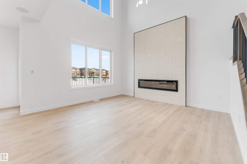 High ceilings with upper transom windows, light wood-finish flooring, and a linear electric fireplace with a tiled surround - 13 Trill Point(E), Spruce Grove, AB 