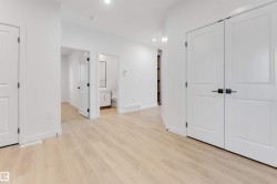 Light wood-finish flooring, white walls, recessed lighting, and white panel doors with matte black hardware - 