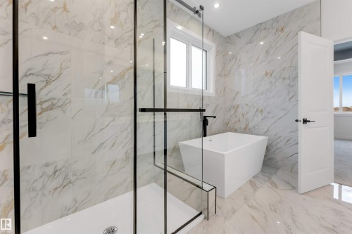 Spacious bathroom featuring a frameless glass shower enclosure, a freestanding soaking tub with a matte black floor-mounted faucet, and marble-look wall and floor tiling - 13 Trill Point(E), Spruce Grove, AB 