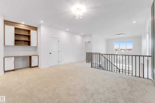 Open concept loft space with built-in desk and cabinetry, carpet flooring, a modern chandelier, and dark metal railings overlooking the level below - 13 Trill Point(E), Spruce Grove, AB 
