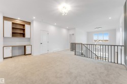 Open concept loft space with built-in desk and cabinetry, carpet flooring, a modern chandelier, and dark metal railings overlooking the level below - 