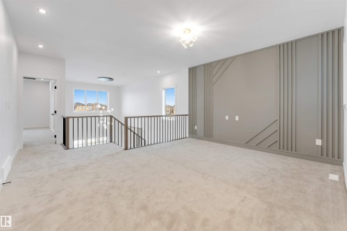 Carpeted area with a decorative accent wall, clear windows, and a metal and wood-finish railing - 13 Trill Point(E), Spruce Grove, AB 