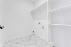 Laundry area with white walls, white trim, white shelving, and marble-patterned flooring - 