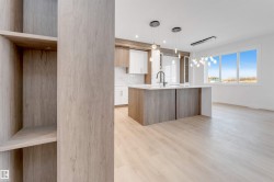 Open-concept living area with light wood-finish flooring, a kitchen island featuring a waterfall countertop and integrated sink, pendant lighting, and abundant natural light from large windows - 