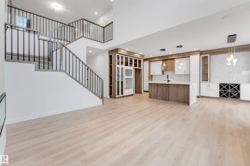 Open-concept living space with light wood-finish flooring, a two-story staircase with dark metal balusters, built-in cabinetry, and integrated kitchen island - 13 Trill Point(E), Spruce Grove, AB 