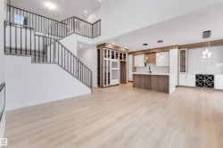 Open-concept living space with light wood-finish flooring, a two-story staircase with dark metal balusters, built-in cabinetry, and integrated kitchen island - 