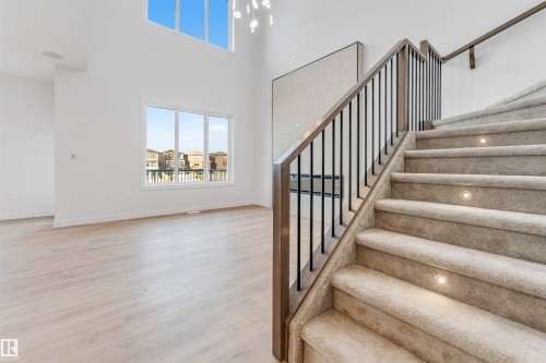 High ceilings, expansive windows, light wood-finish flooring, carpeted staircase with integrated step lighting, and dark metal balusters - 13 Trill Point(E), Spruce Grove, AB 