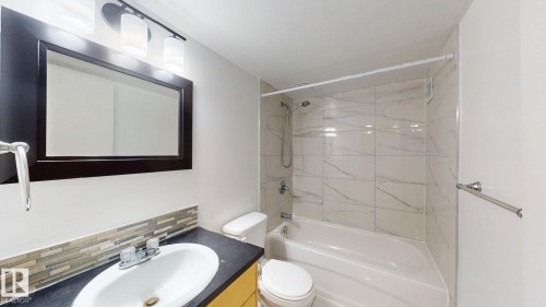 Bathroom featuring a vanity with a dark countertop, white oval sink, and a mosaic tile backsplash - #307 10140 120 Street Nw, Edmonton, AB - Indoor Photo Showing Bathroom