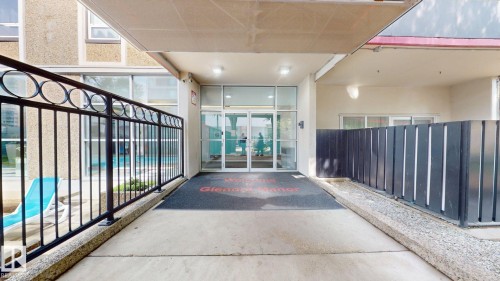 Covered entrance featuring glass double doors, overhead lighting, concrete walkway, and black metal railing - #307 10140 120 Street Nw, Edmonton, AB - Indoor Photo Showing Other Room
