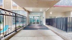 Covered entrance featuring glass double doors, overhead lighting, concrete walkway, and black metal railing - 