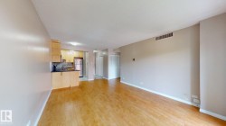 Open-concept living space featuring wood-finish flooring, a recessed ceiling, and a kitchen area with light wood cabinetry, a dark countertop, and a tiled backsplash - 