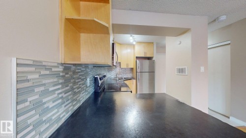 Kitchen featuring dark countertops, a mosaic tile backsplash, light wood cabinetry, a stainless steel refrigerator, and a black range - #307 10140 120 Street Nw, Edmonton, AB - Indoor Photo Showing Kitchen
