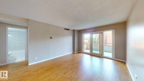 Spacious living area featuring wood-finish flooring, light neutral wall paint, and a textured ceiling - #307 10140 120 Street Nw, Edmonton, AB - Indoor Photo Showing Other Room