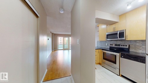 Modern kitchen featuring stainless steel appliances, light wood-finish cabinetry, dark countertops, and a mosaic tile backsplash - #307 10140 120 Street Nw, Edmonton, AB - Indoor Photo Showing Kitchen