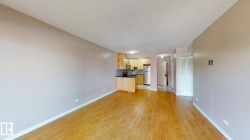 Open-concept living space featuring wood-finish flooring, light-toned walls, recessed lighting, and a kitchen with wood cabinetry, dark countertops, and stainless steel appliances - 