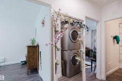Stacked laundry appliances, wood-finish flooring, white walls, and bright overhead lighting - 