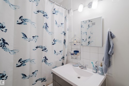 White tile walls, vanity with integrated sink, rectangular mirror, and an overhead light fixture - 11134 11138 116 Street Nw, Edmonton, AB 