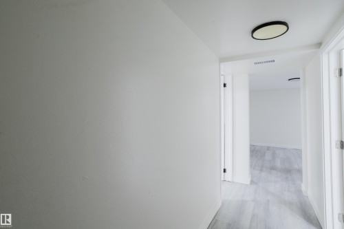 Hallway featuring flush-mount ceiling lighting, crisp white paint, and wood-finish flooring - 11134 11138 116 Street Nw, Edmonton, AB 