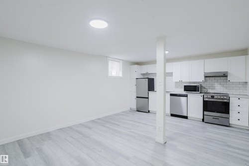 Kitchenette with white cabinetry, stainless steel appliances, white subway tile backsplash, and wood-finish flooring - 11134 11138 116 Street Nw, Edmonton, AB 
