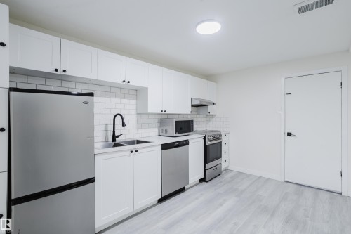 White shaker-style cabinetry with black hardware, stainless steel appliances, subway tile backsplash, and light wood-finish flooring - 11134 11138 116 Street Nw, Edmonton, AB 