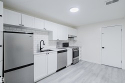 White shaker-style cabinetry with black hardware, stainless steel appliances, subway tile backsplash, and light wood-finish flooring - 