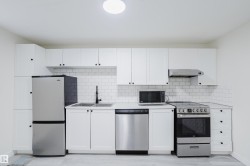 White shaker cabinetry with dark hardware, stainless steel appliances, dual basin sink with matte black faucet, white subway tile backsplash, and light-toned flooring - 