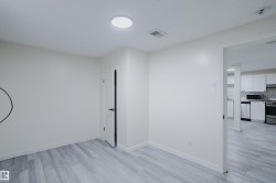 Recessed ceiling light, light wood-finish flooring, white walls, and a white interior door with black hardware - 