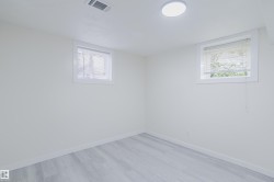 Light-toned wood-finish flooring, two rectangular windows with blinds, a white ceiling, and a flush-mount overhead light fixture - 