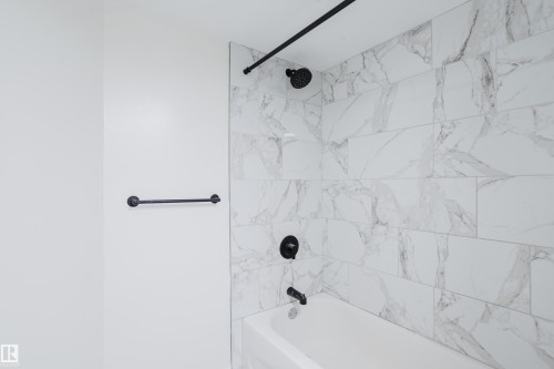 Tub and shower combination featuring large format tile surround, matte black fixtures, and a coordinating towel bar - 11134 11138 116 Street Nw, Edmonton, AB 