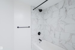 Tub and shower combination featuring large format tile surround, matte black fixtures, and a coordinating towel bar - 