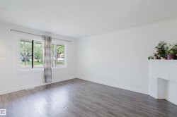 Spacious room featuring light gray wood-finish flooring, a white-painted fireplace, and a large window with white trim - 