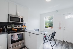 Kitchen featuring stainless steel appliances, white cabinetry, dark countertop, and wood-finish flooring - 