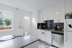 White cabinetry, undermount stainless steel sink, stainless steel dishwasher, grey textured backsplash, and light wood-finish flooring - 