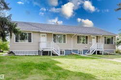 Beige horizontal siding exterior with a dark shingle roof, multiple white-trimmed windows, and two entryways with white staircases - 