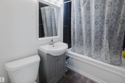 Full bathtub with shower, dark tile shower surround, vanity with integrated sink, chrome faucet, and wood-finish flooring - 11134 11138 116 Street Nw, Edmonton, AB 