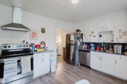 Kitchen featuring white cabinetry, wood-finish flooring, stainless steel appliances, and a black tile backsplash - 
